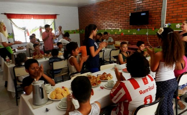 Em uma sala, crianças sentadas em várias mesas