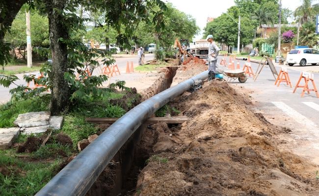 Buraco estreito e cumprido aberto ao lado de um rua com terra ao lado e grande tubulação preta