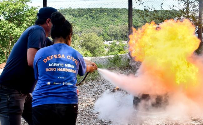 Uma menina e um instrutora com um extintor apagando um fogo provocado em um tambor