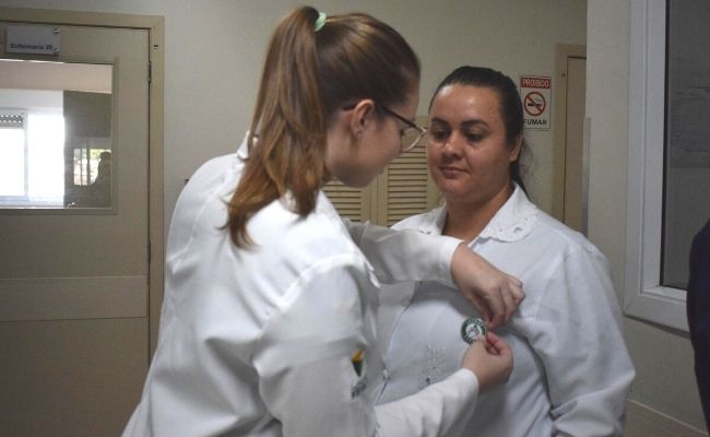 Duas mulheres de branco, uma colocando um boton na outra
