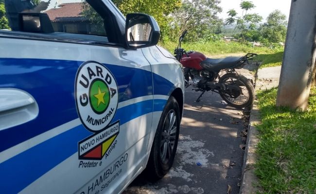 Carro com a insígna da guarda municipal na porta e moto estacionada a frente