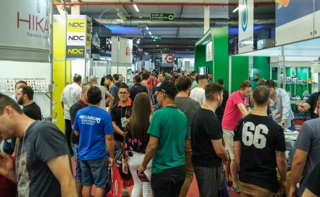 Corredor da feira cheio de pessoas, com estandes nos dois lados