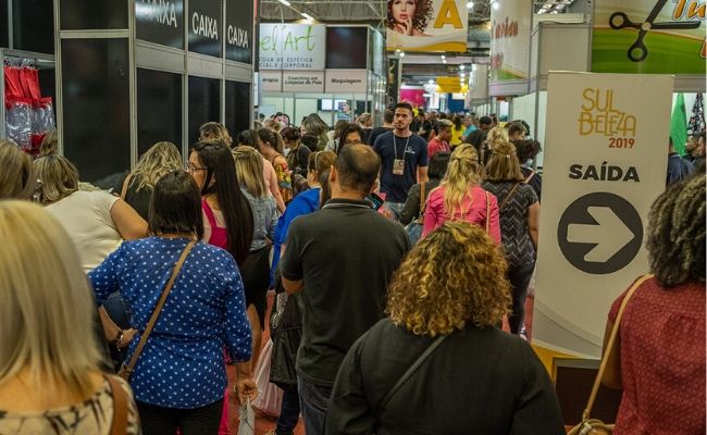 Corredor da feira cheio de pessoas, com estandes nos dois lados