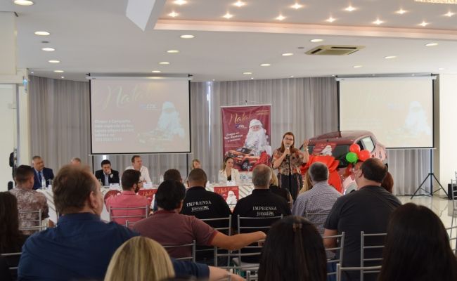 Prefeita Fátima em pé ao fundo ao microfone. Atrás da prefeita, uma mesa com pessoas sentadas. À frente da prefeita, público sentado.