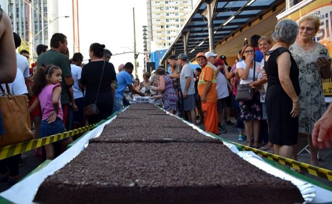 Bolo de chocolate de sete metros em cima de uma mesa e pessoas ao redor