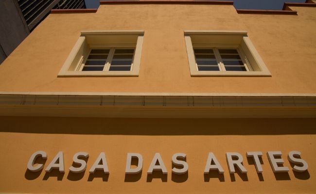 Fachada da Casa das Artes, que é um prédio amarelo e as letras escritas em branco