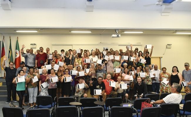 Em um auditório, grupo de formandos em pé segurando o diploma
