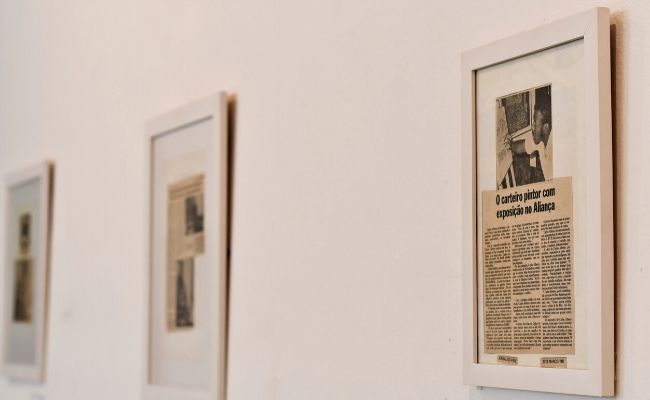 Em uma parede branca, três quadros pendurados com reportagem do Carlão