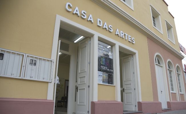 Fachada da Casa das Artes, que é um prédio amarelo e as letras escritas em branco