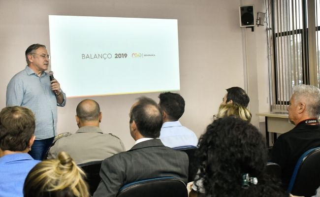 Na imagem uma sala com pessoas sentadas em cadeiras e ao fundo o secretário Roberto em pé ao microfone