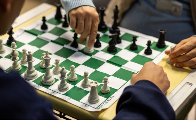 A imagem mostra um tabuleiro de xadrez com duas pessoas jogando