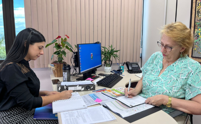 Duas mulheres sentadas à mesa em um escritório com papeis e documentos