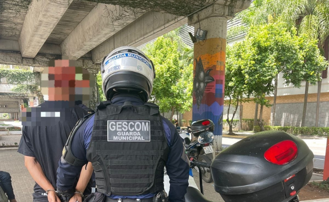 Guarda municipal de costas e o homem foragido algemado, também de costas