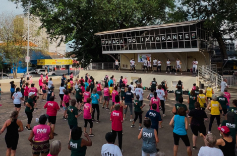 Mega aula de dança na Praça do Imigrante, na área central da cidade, com um grande número de participantes da melhor idade usando camisetas coloridas da PMI