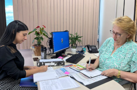 Duas mulheres sentadas à mesa em um escritório com papeis e documentos